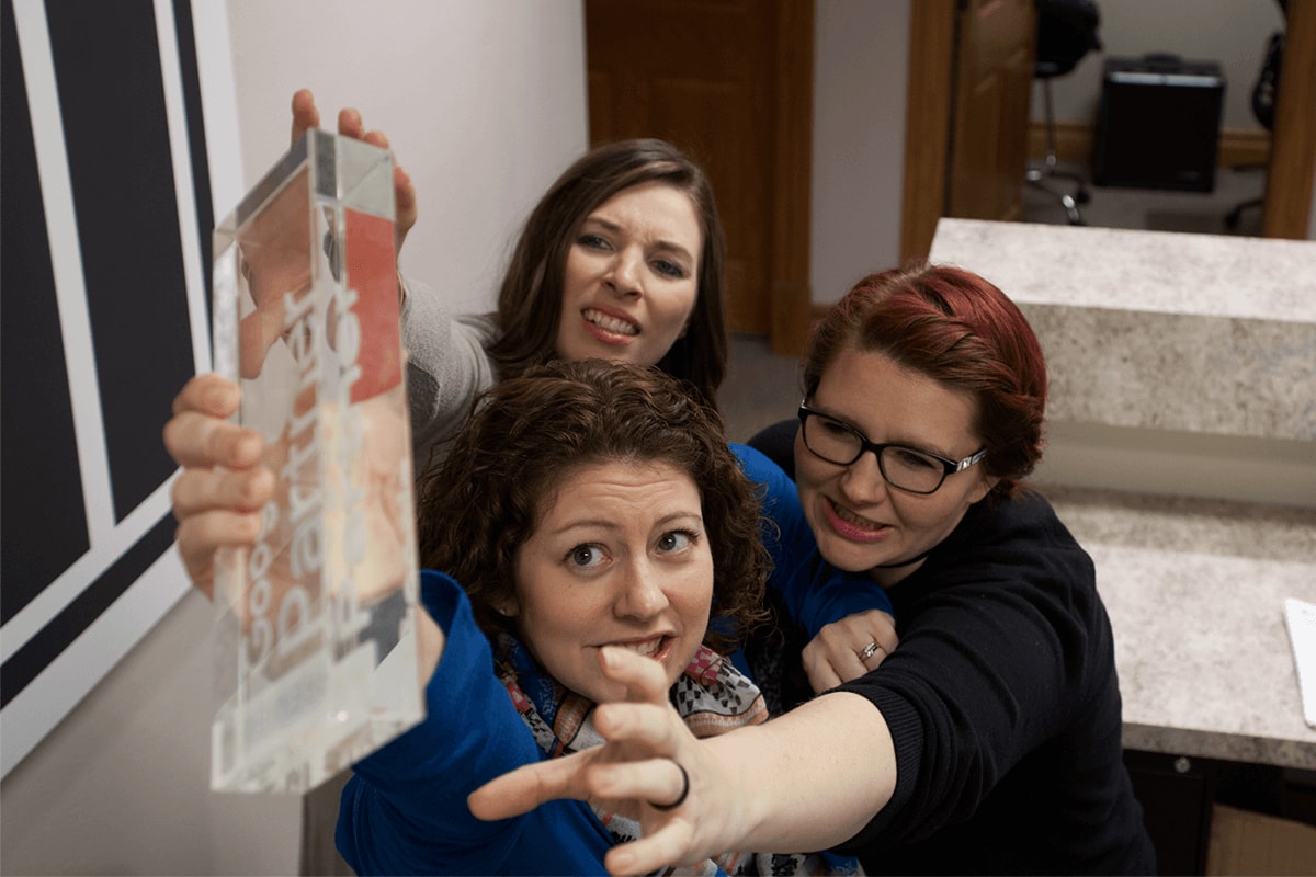 Google certified Ramsey MediaWorks employees reaching upwards for the Google Premier Partner desk plaque.