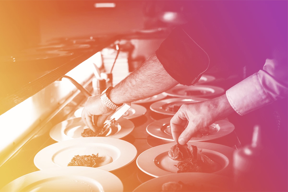 Two people grabbing food from a buffet table.